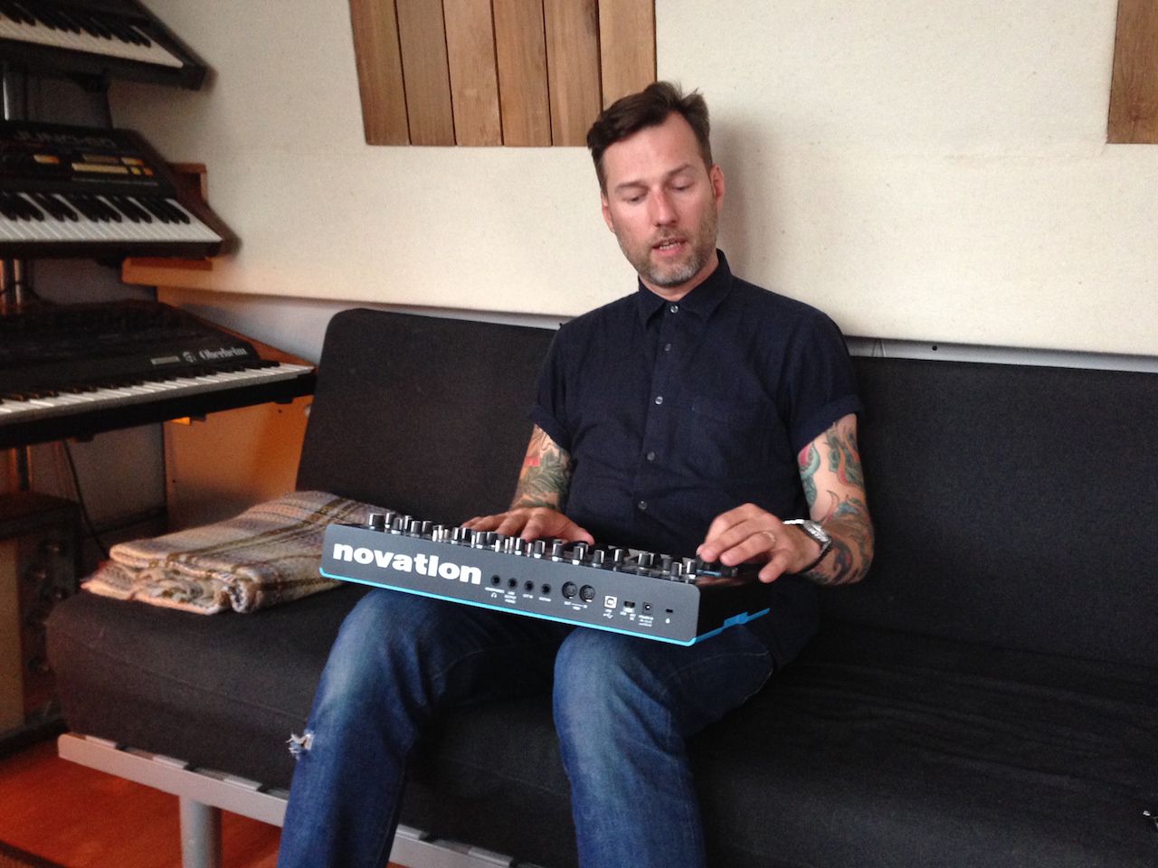 Liam Howe shows off his Novation Bass Station upon a comfy couch!